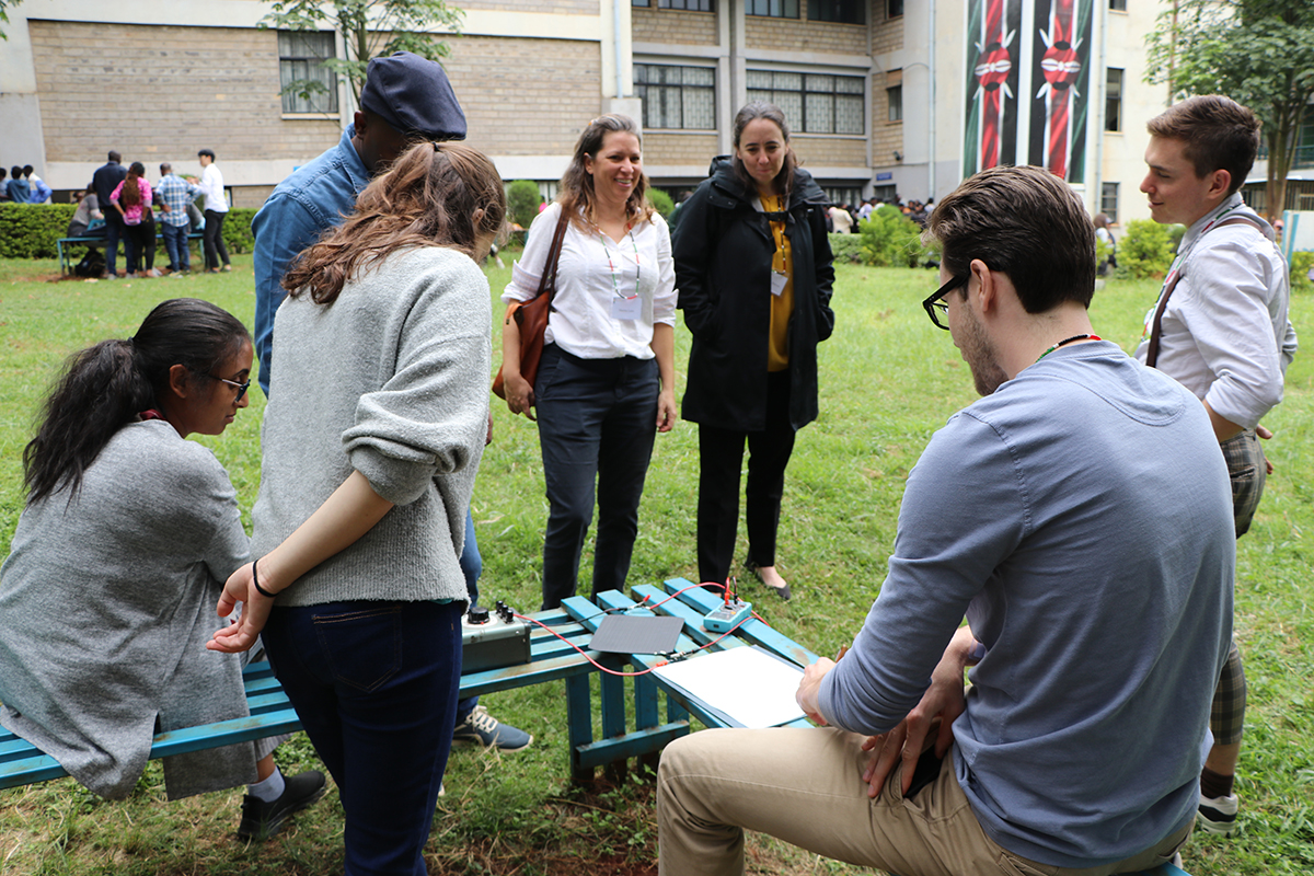 People gather outside near green blue benches with wires attached to machines