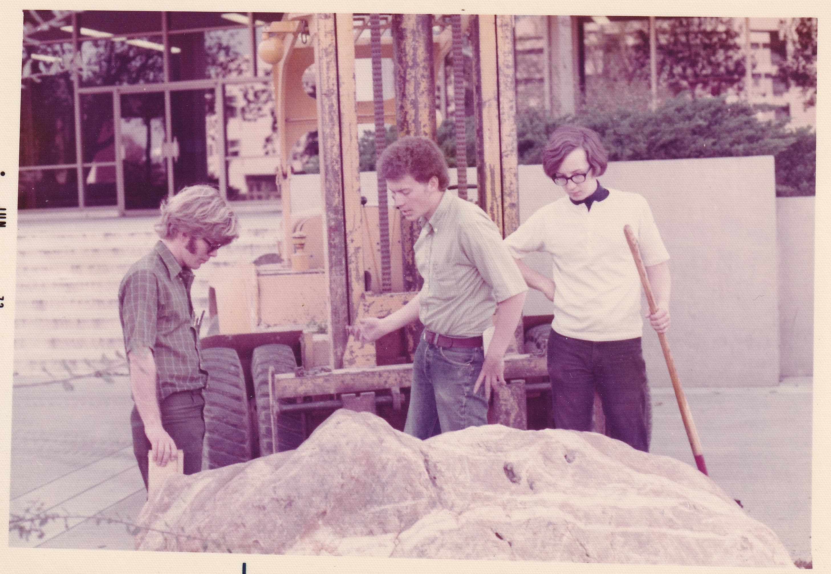 Three UCD students stand near a rock and forklift