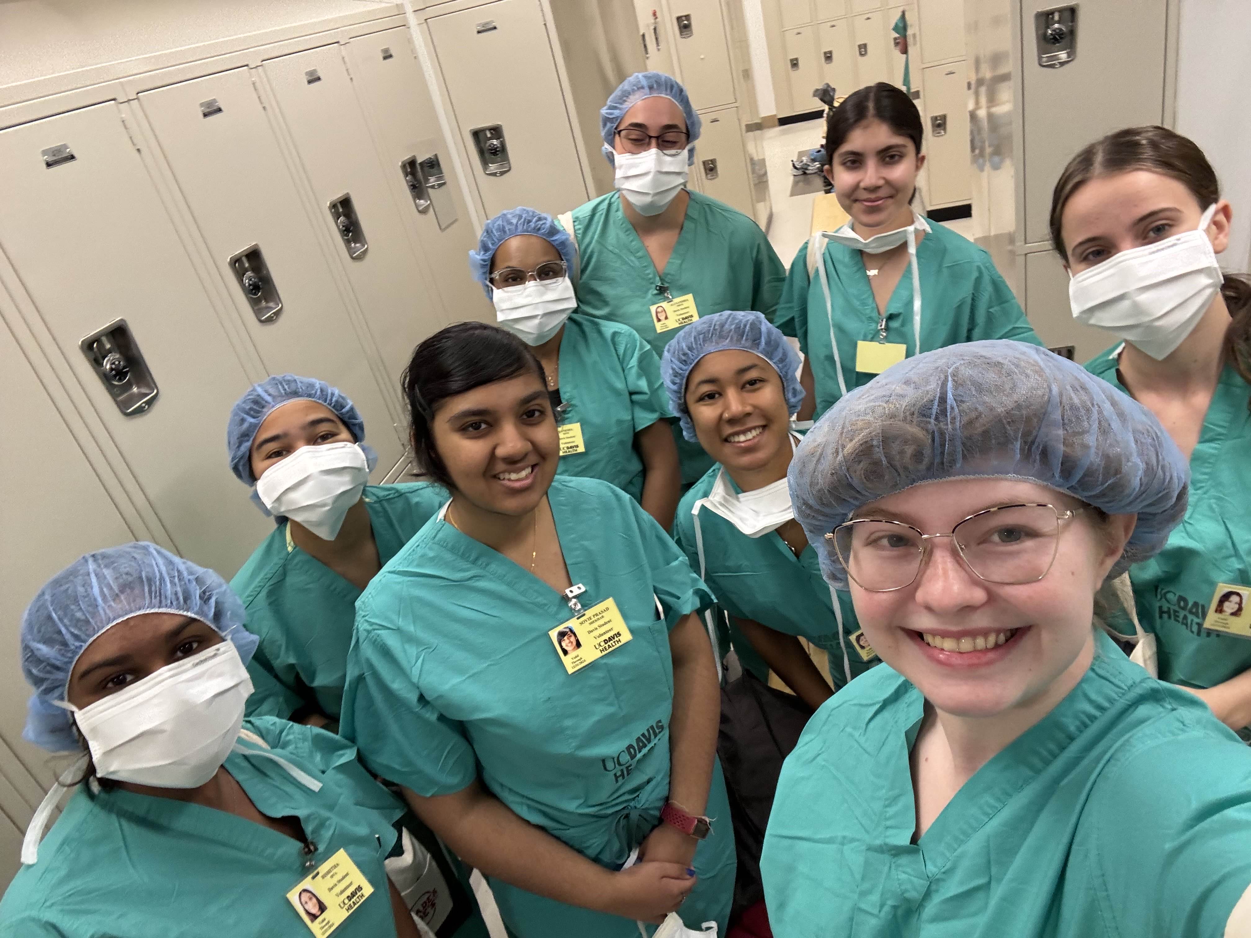 A group of students in scrubs, hair nets, and masks taking a selfie