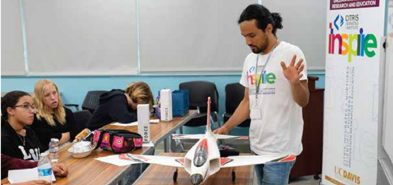 CITRIS INSPIRE team member stands at front of classroom near a model plane in front of students