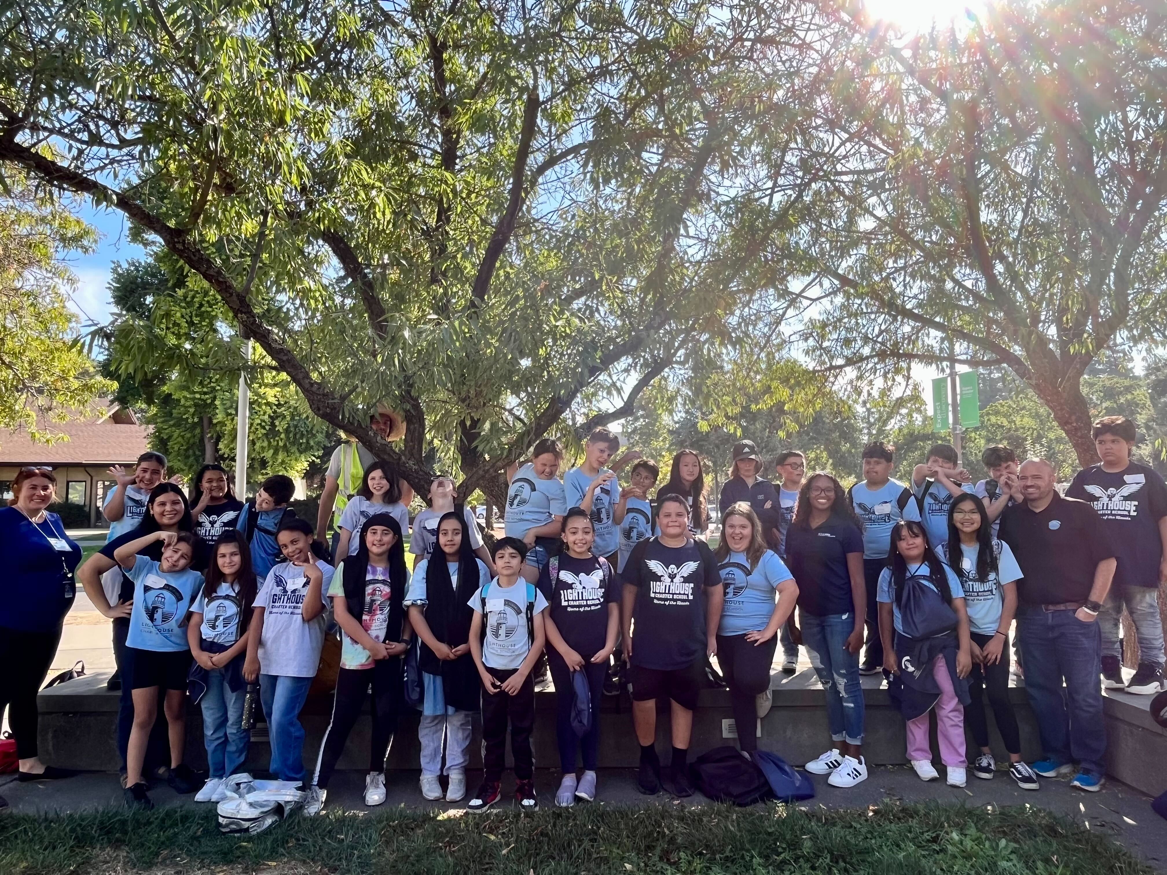 A handful of young students stand on the UC Davis campus with a tour guide and teachers