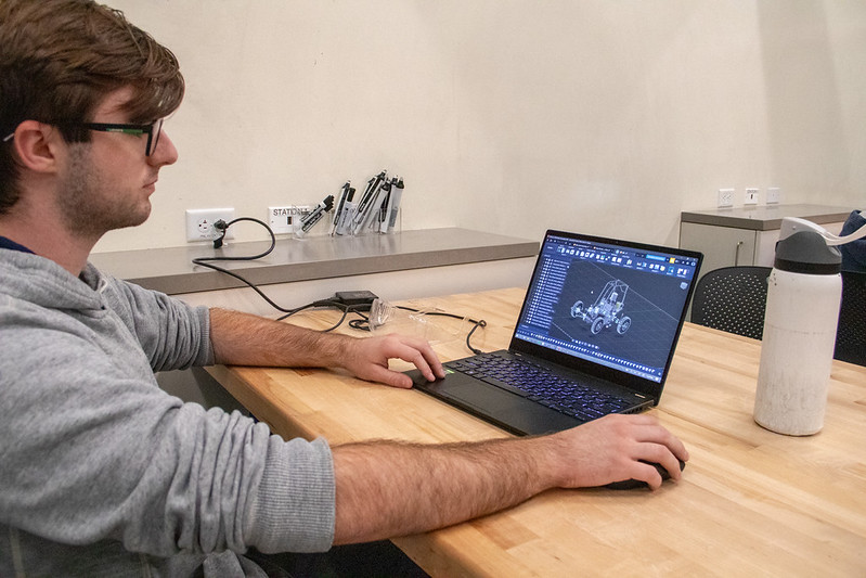 A person working on a laptop showing a 3D model of an off-road car