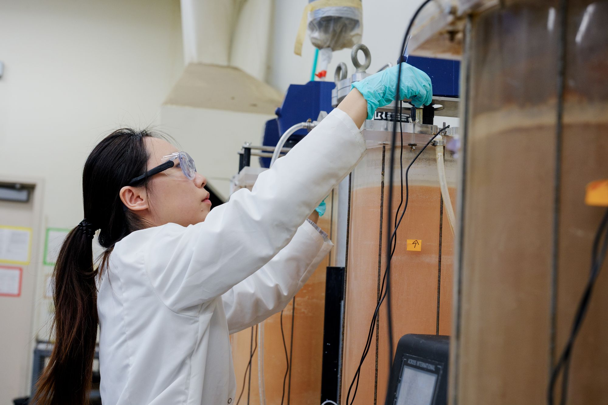 Scientist in white coat adjusts tall glass lab apparatus 