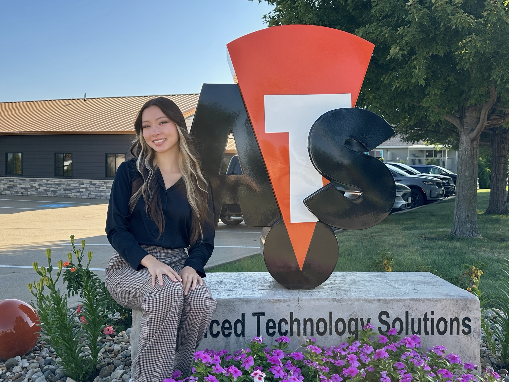 Pham seated beside a colorful company logo sign, flowers and building behind