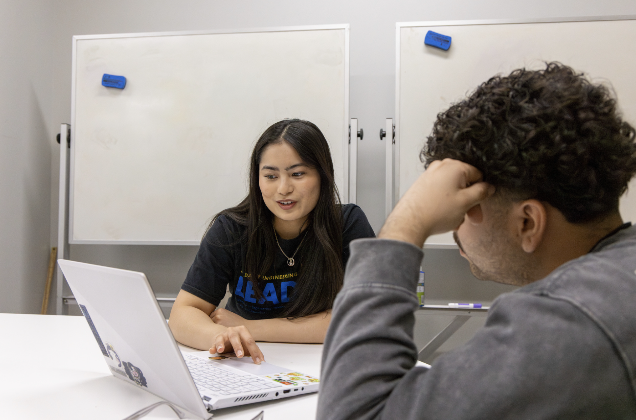 de Leon assists a student with a laptop in a meeting room.