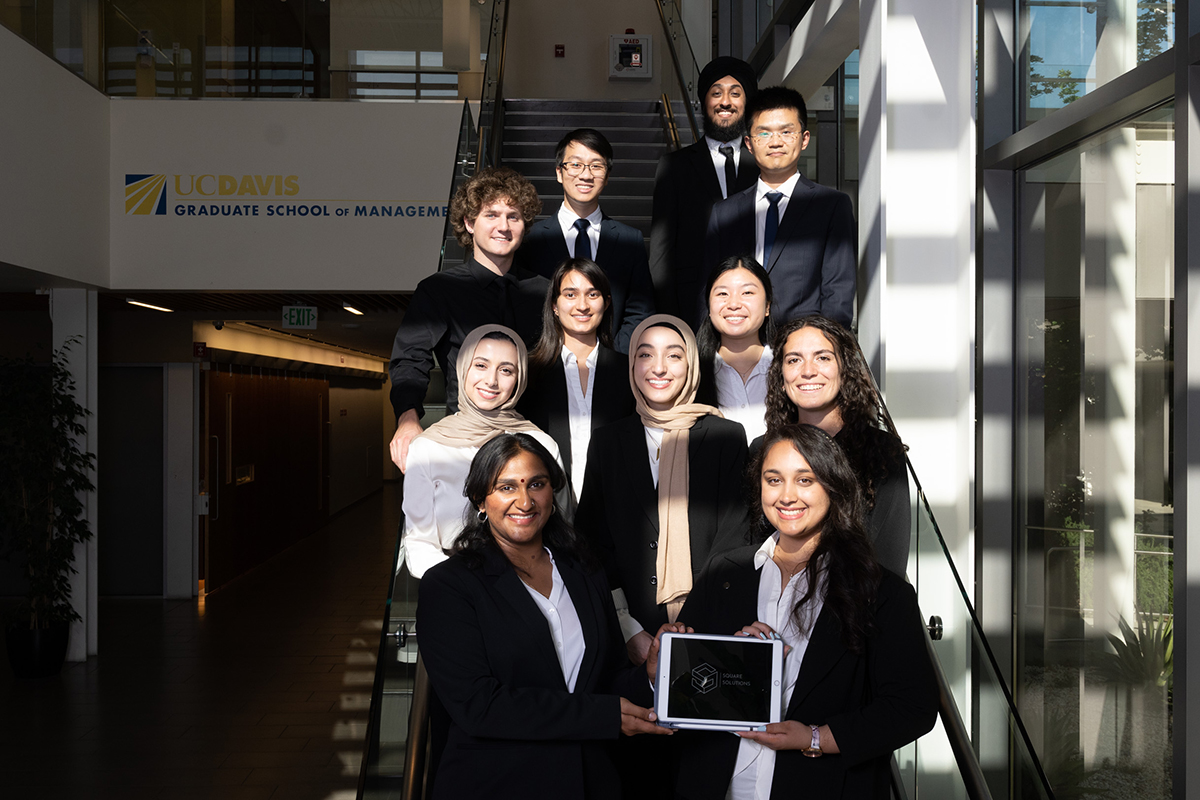 large group of undergraduates in business attire on a staircase with laptop screen showing their startup