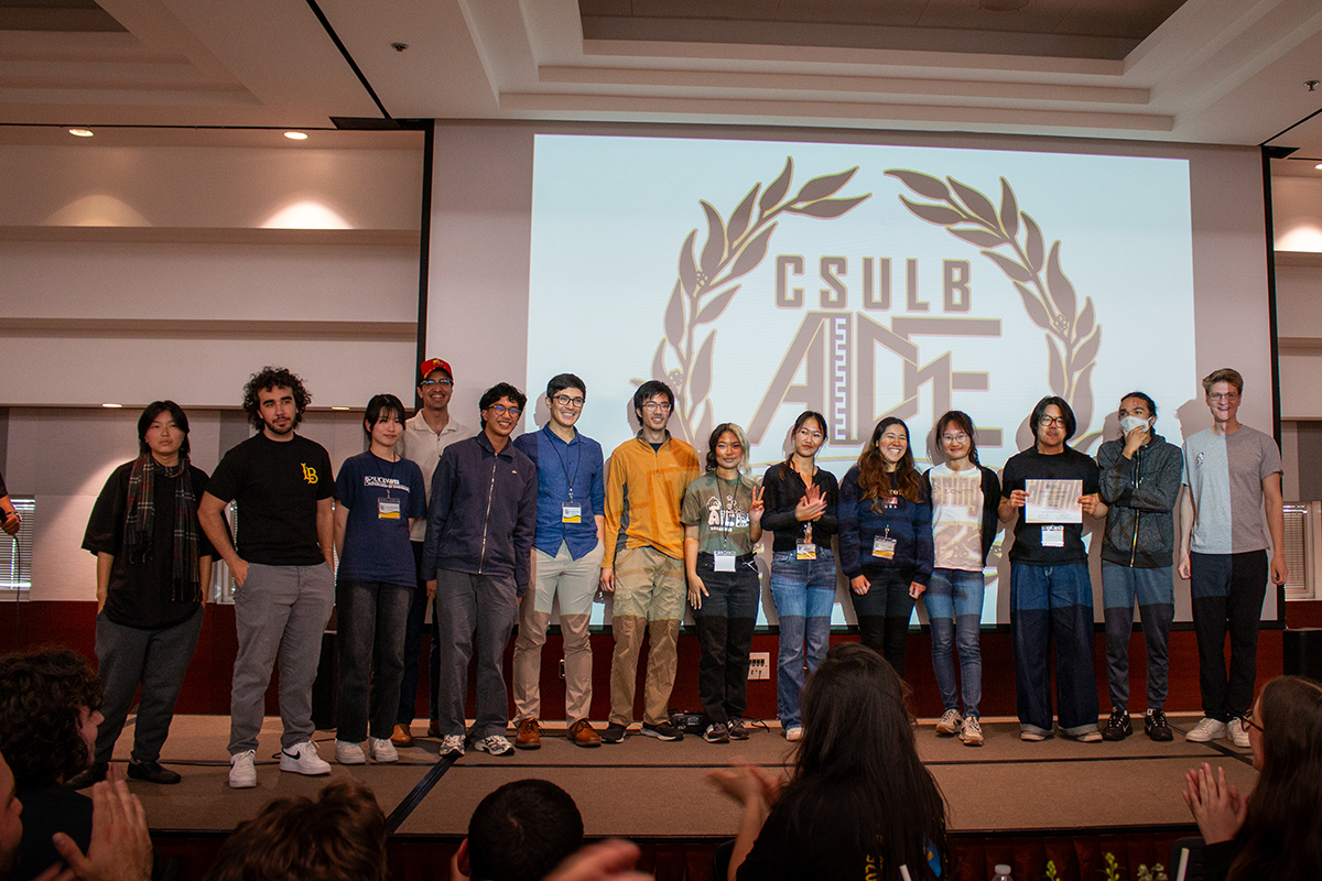 Group members stand together on stage in front of a projector, accepting an award