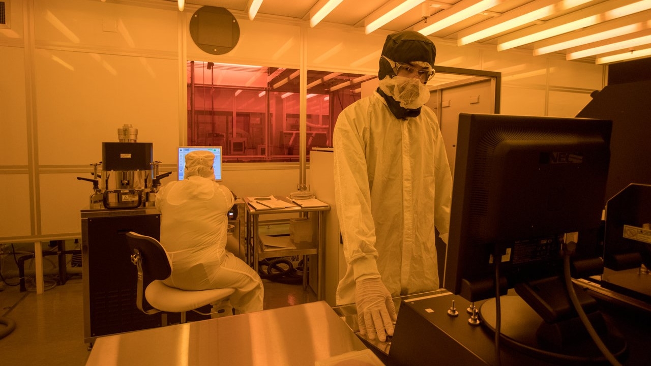 Two cleanroom users in a tinted room for photolithography. The yellow lights protect photo-sensitive samples from exposure to fluorescent light. Photo: Lucy Knowles/UC Davis. uc davis engineering center nano micro manufacturing cnm2