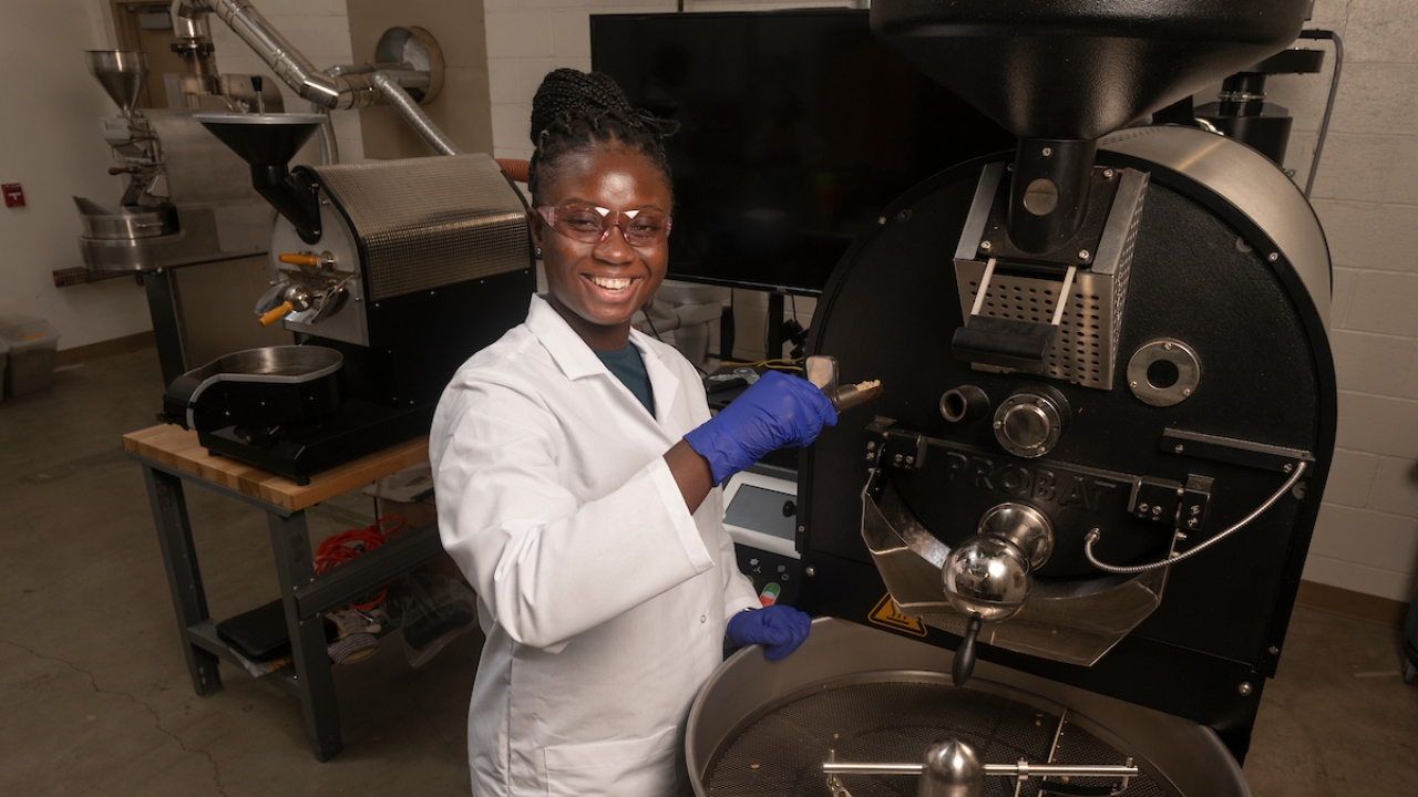 Laudia Anokye-Bempah stands in front of a coffee roaster