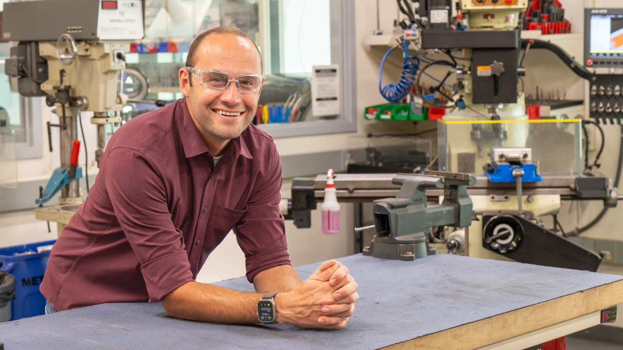 A man in a button up leans on a workbench