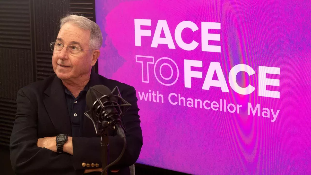 Stephen Robinson sits in front of a purple screen that reads Face to Face with Chancellor May
