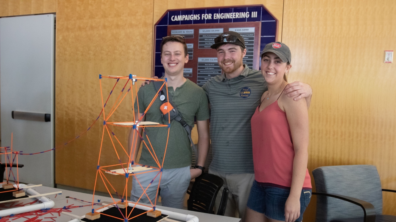Three people posing for a picture behind a building structure display