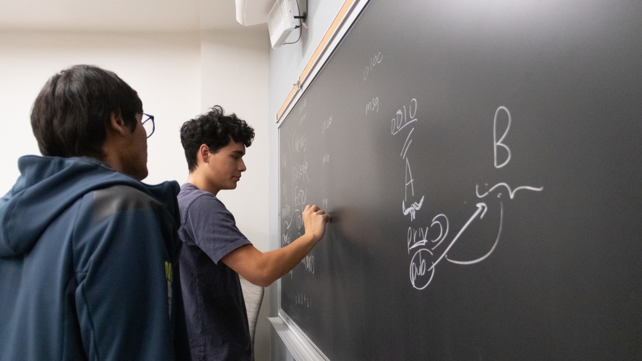 Two Quantum Computing at Davis Club members stand at chalkboard