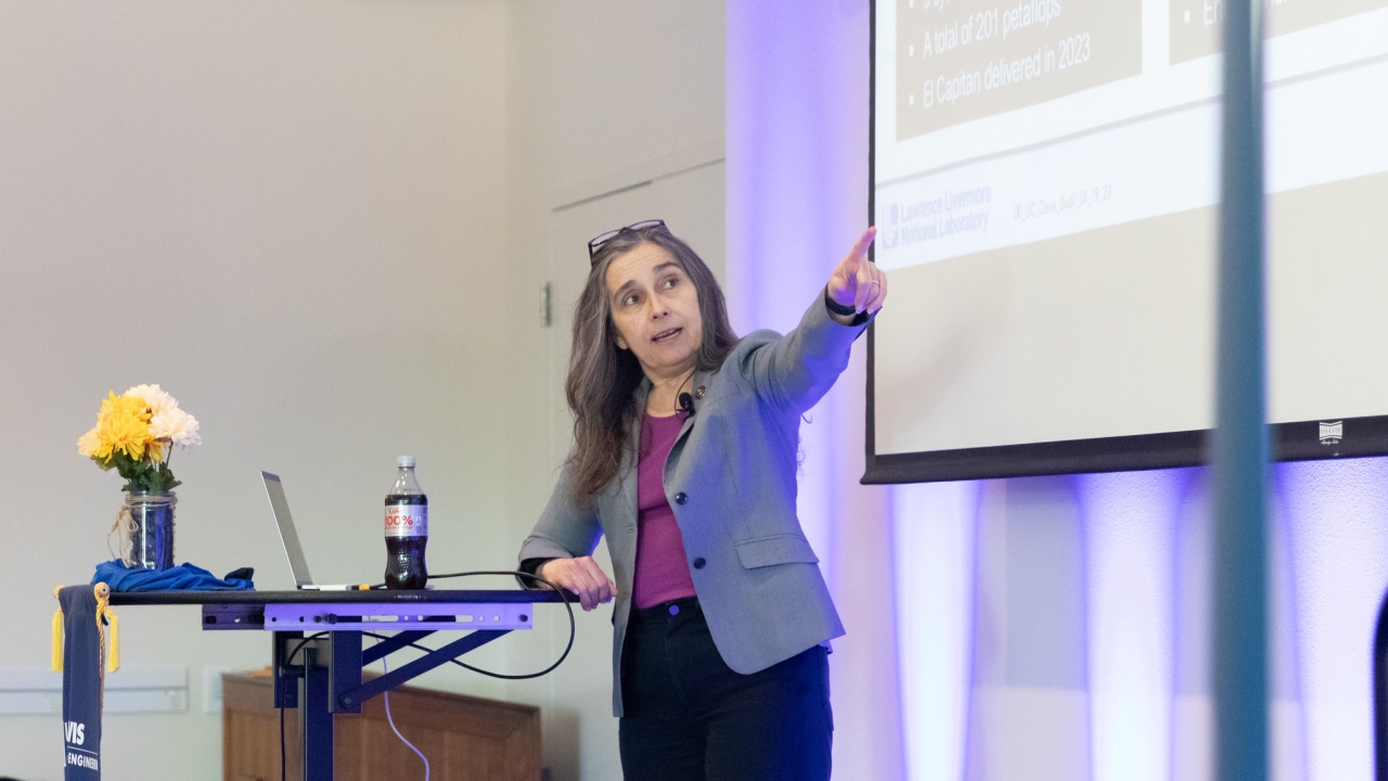 Kim Budil on stage at a UC Davis College of Engineering event, pointing to a projector slideshow.