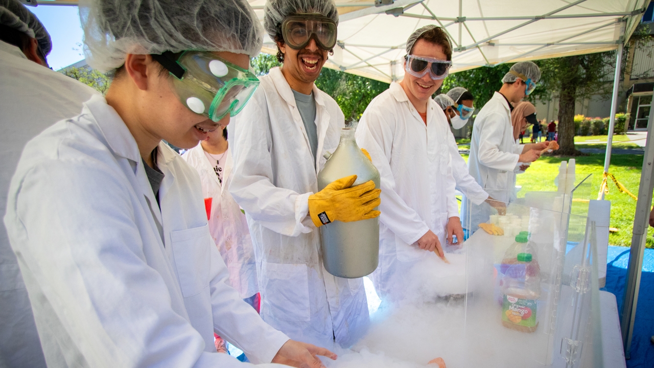 Three students in lab coats handling liquid nitrogen
