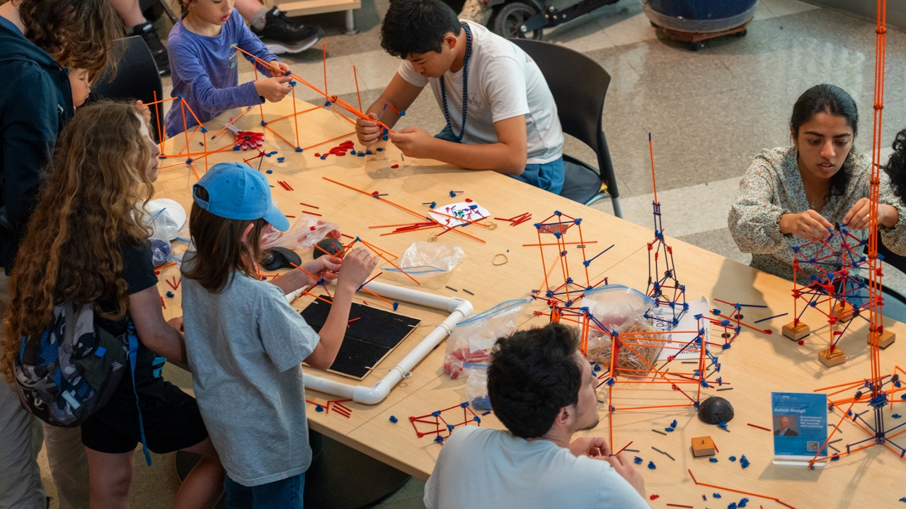 Children and adults engaged in building projects at a table filled with model construction materials.