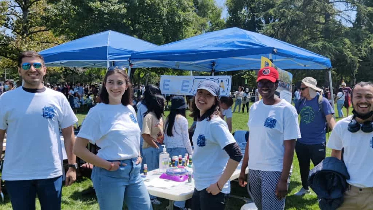 People wearing white shirts in front of pop up tents at an outdoor UC Davis Picnic Day event