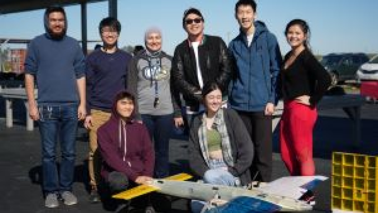 Eight students stand next to a model plane 