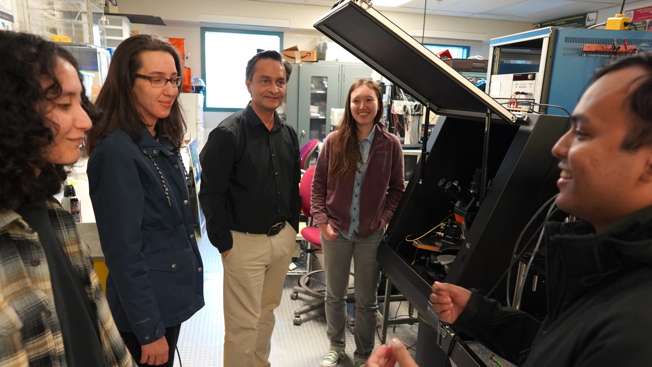 Saif Islam stands with students near machinery in a lab