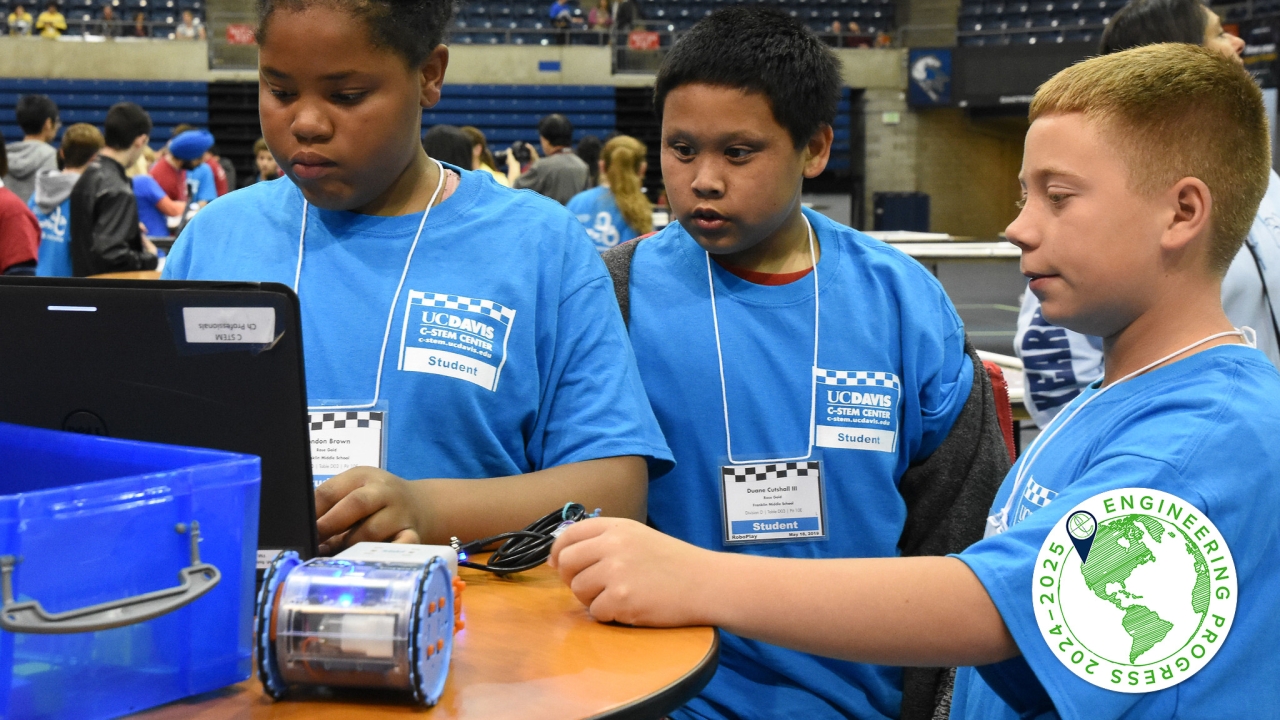 Three students stand together, looking at a laptop