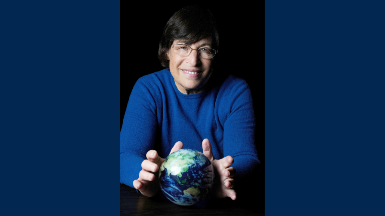 Lynn Rothschild holding a small Earth globe against dark background
