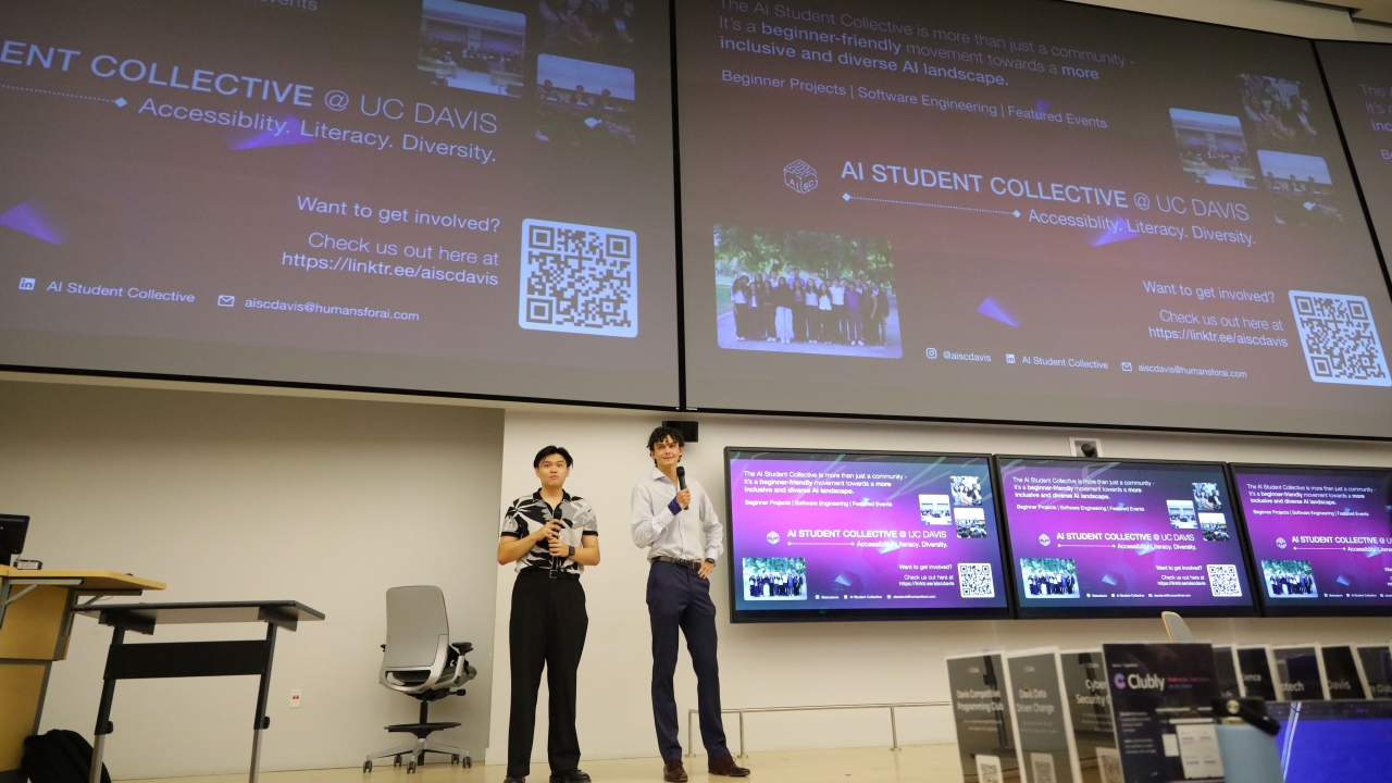 Two students presenting in front of two giant screens