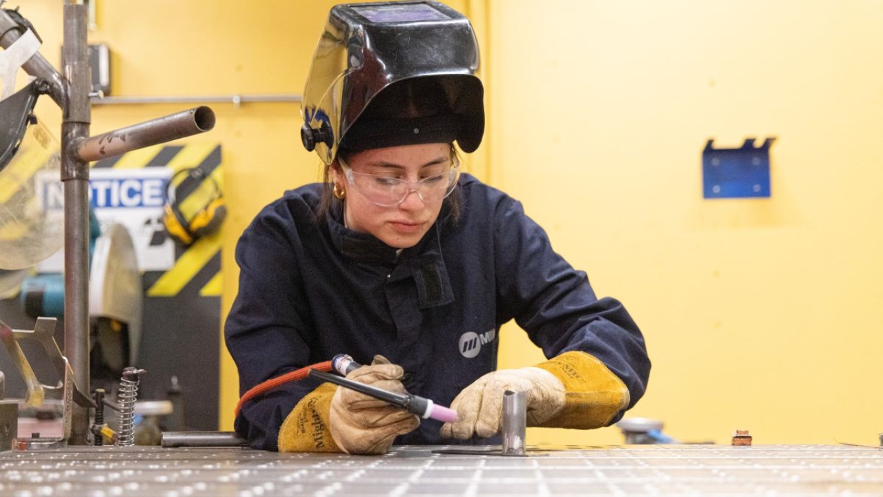 Lena Araya in protective gear works on a metal surface with welding equipment.