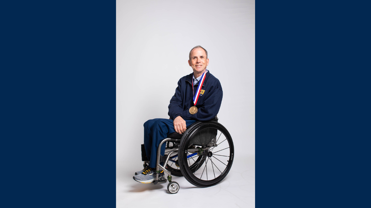 Man seated in wheelchair wearing a medal, studio photo