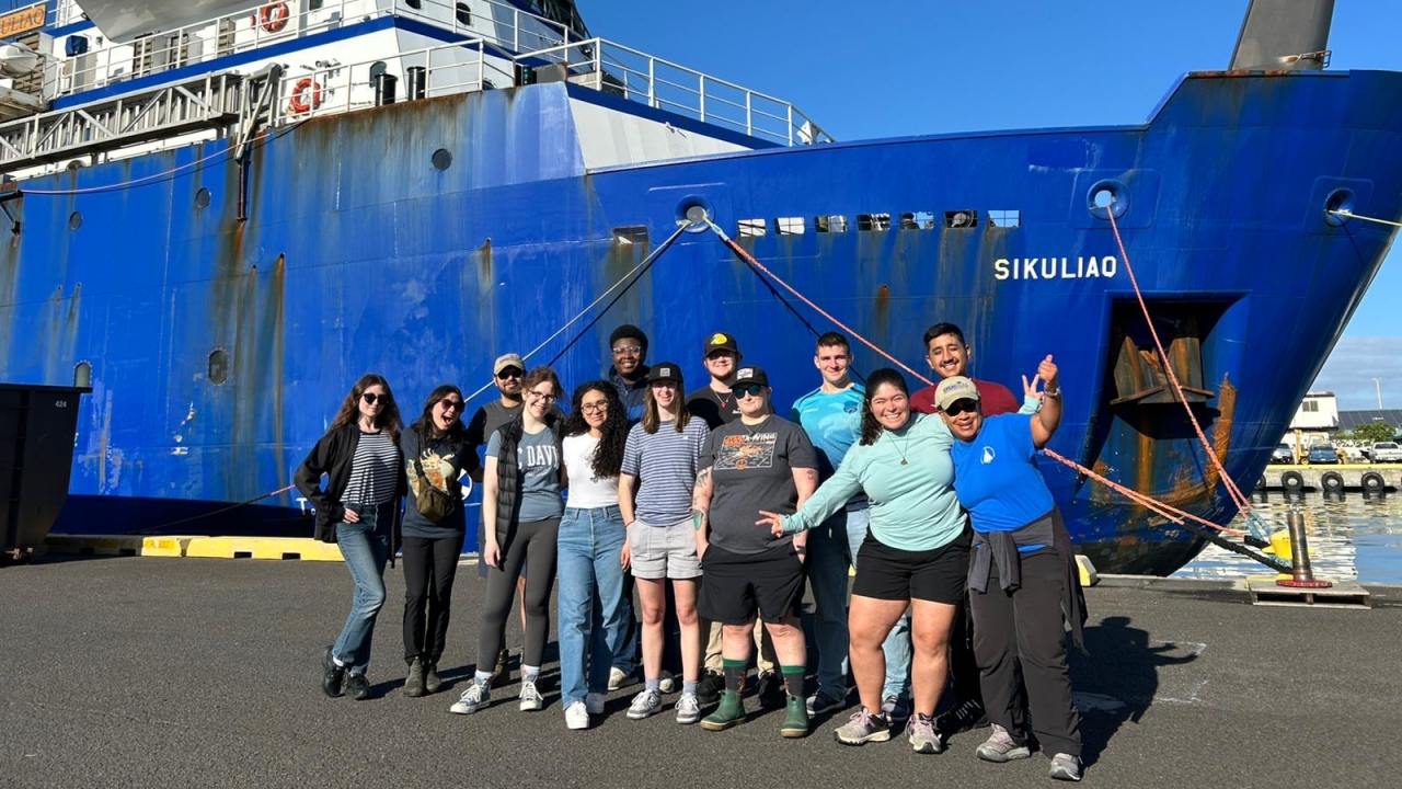 A group of people posing for a picture in front of a large blue boat