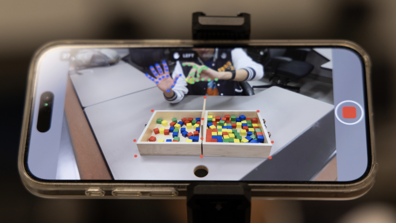 A smartphone displays a program tracking hands moving small colorful blocks.