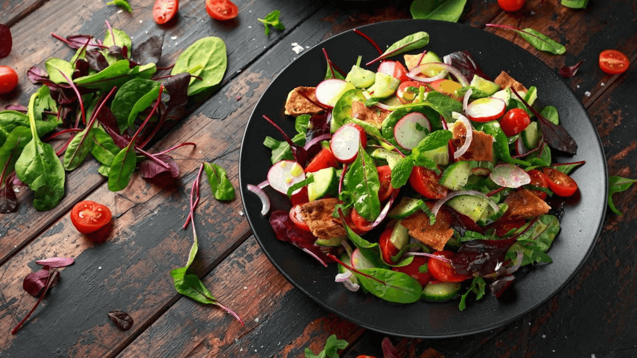 Colorful salad with cherry tomatoes, cucumber, radish and greens in black bowl on dark wood
