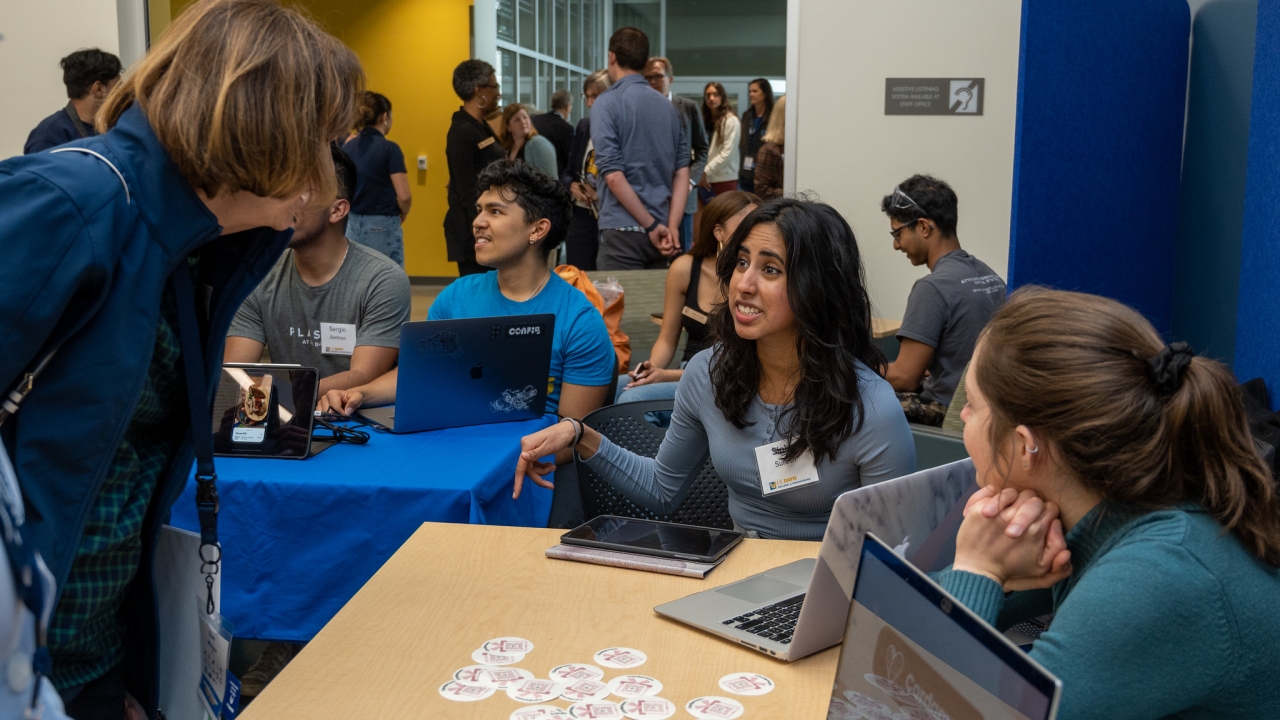 Student start up teams from UC Davis Engineering sit at tables in the Engineering Student Design Center and talk with event goers for the grand opening