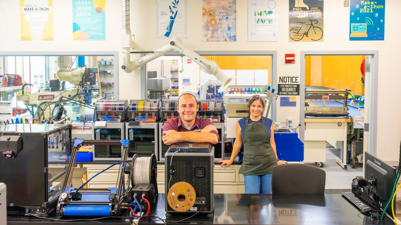A man and women stand in a room full of 3D printers and other machines