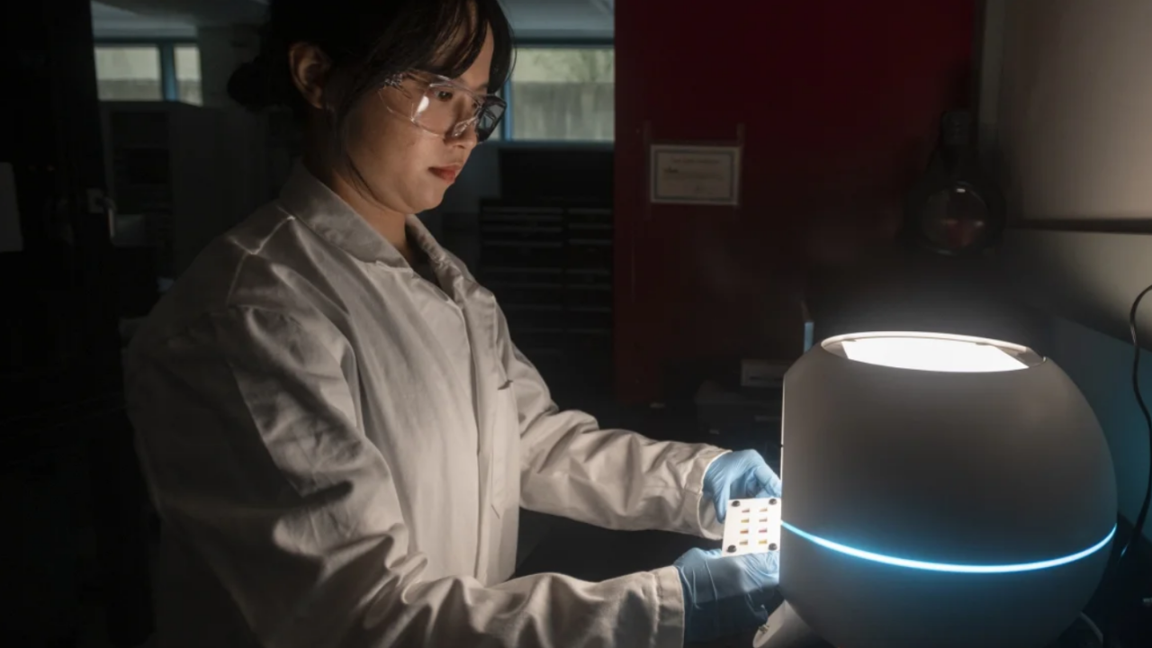 Person wearing PPE stands near circular machine with white and blue lights