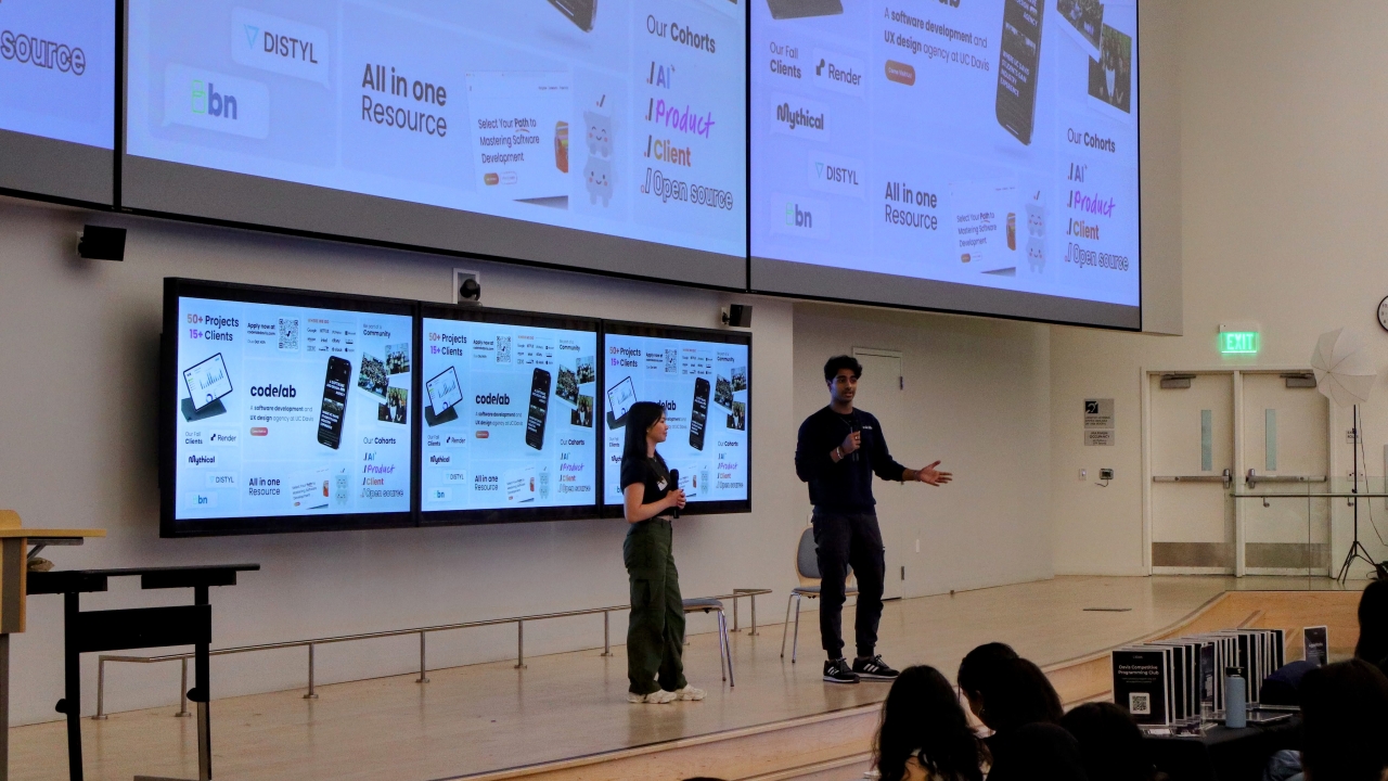 Two students speaking into microphones in front of giant screens