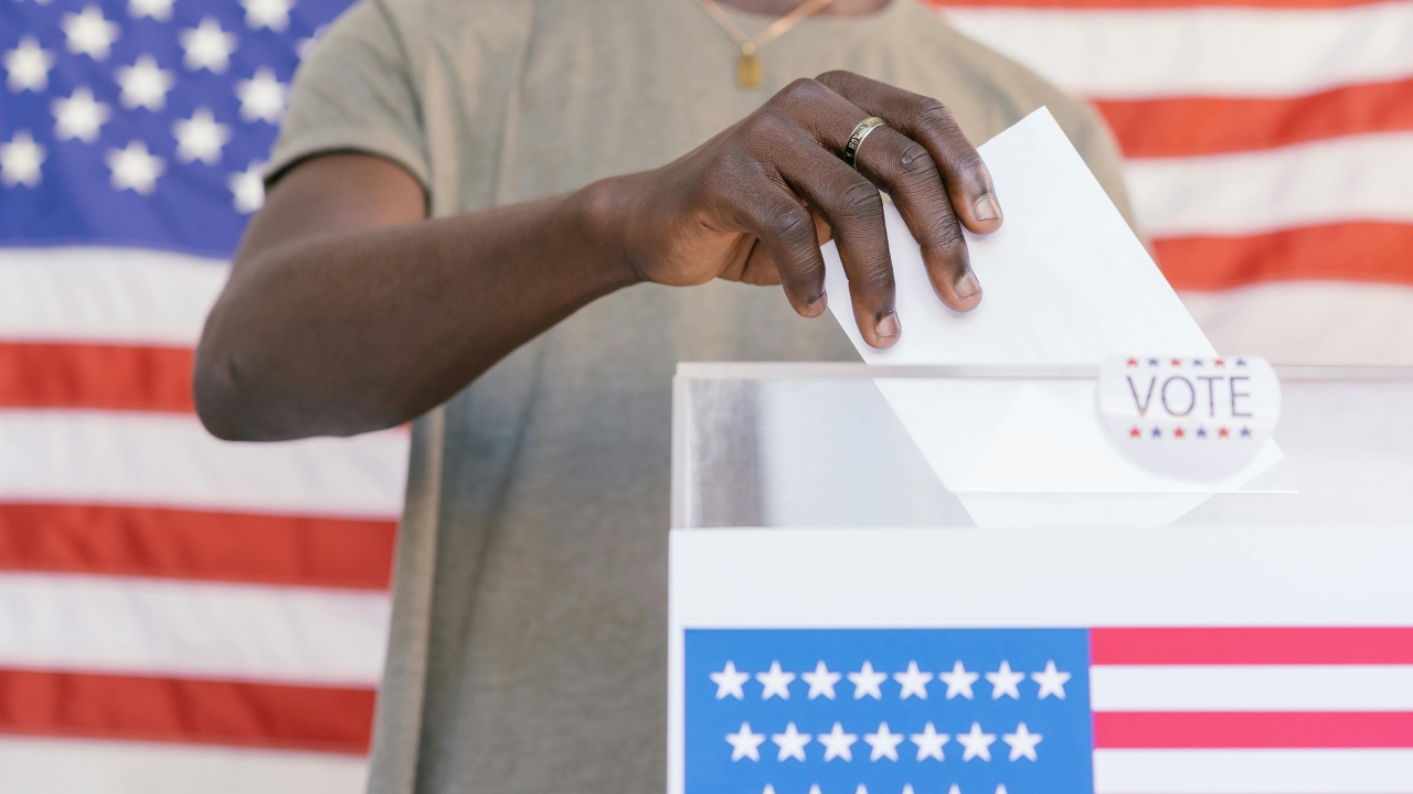 Person places ballot in box, American flags are seen on the box and in the background