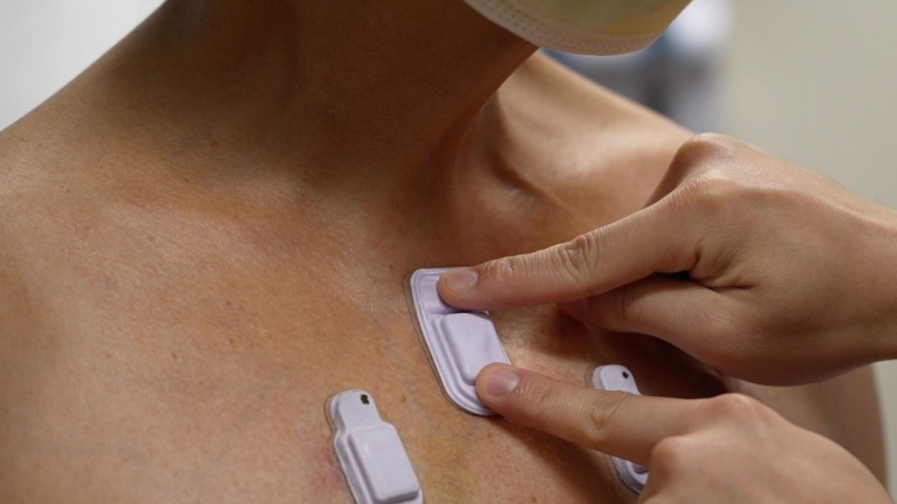Person's body with three white wearable devices on it, one being pressed down by two fingers