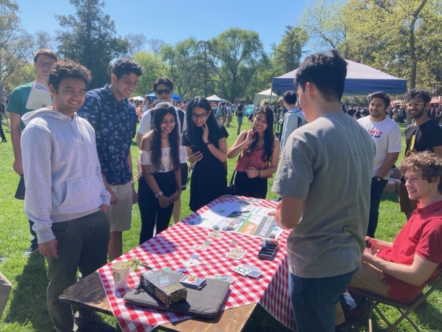 UC Davis students gather around a table at an outdoor event. The table has a picnic blanket and poker chips and cards laid out.