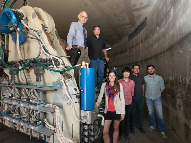 Seven people stand inside a concrete tunnel beside a large blue and white industrial machine