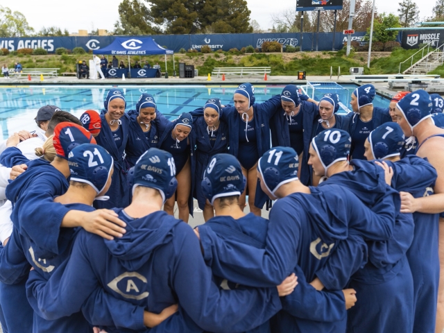 Many members of UC Davis Womens Water Polo team huddle near a pool