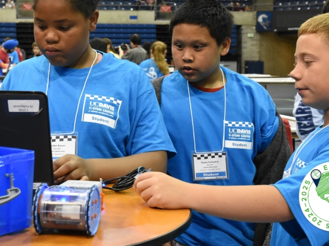 Four boys in blue UC Davis C-STEM Center Student shirts looking at a laptop