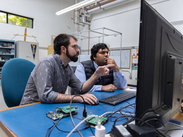 UC Davis graduate students Adam Zufall and Ayush Patnaik sit at a desk working on a payload