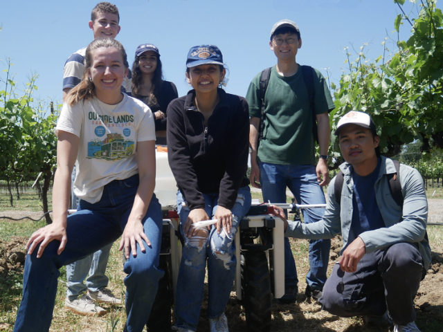 Students stand in field with a robot