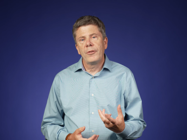 Simon Cherry against a blue gradient background in a filming studio