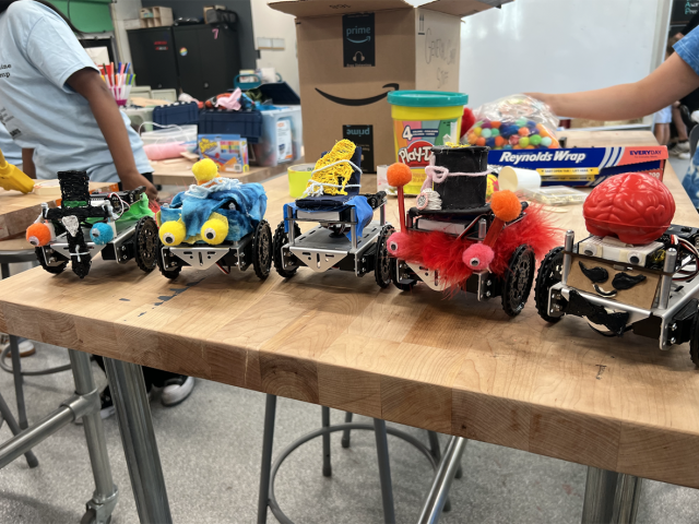 Five small robots decorated by young students sit on a table in a classroom