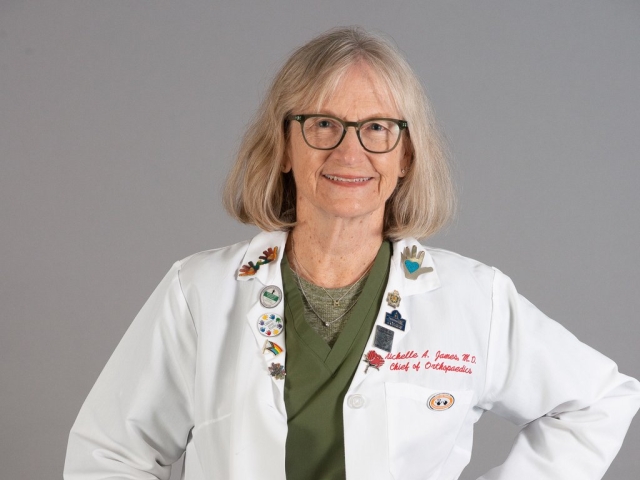 Michelle James, M.D., chief of orthopedics at Shriner's Children's Northern California wears a white lab coat and stands against a gray background