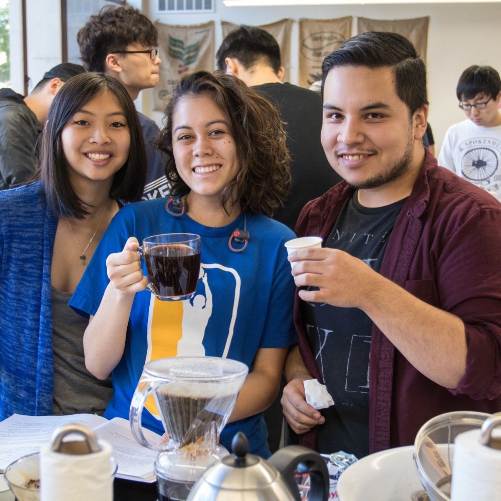 Three students hold up coffee cups in Coffee Center Lab