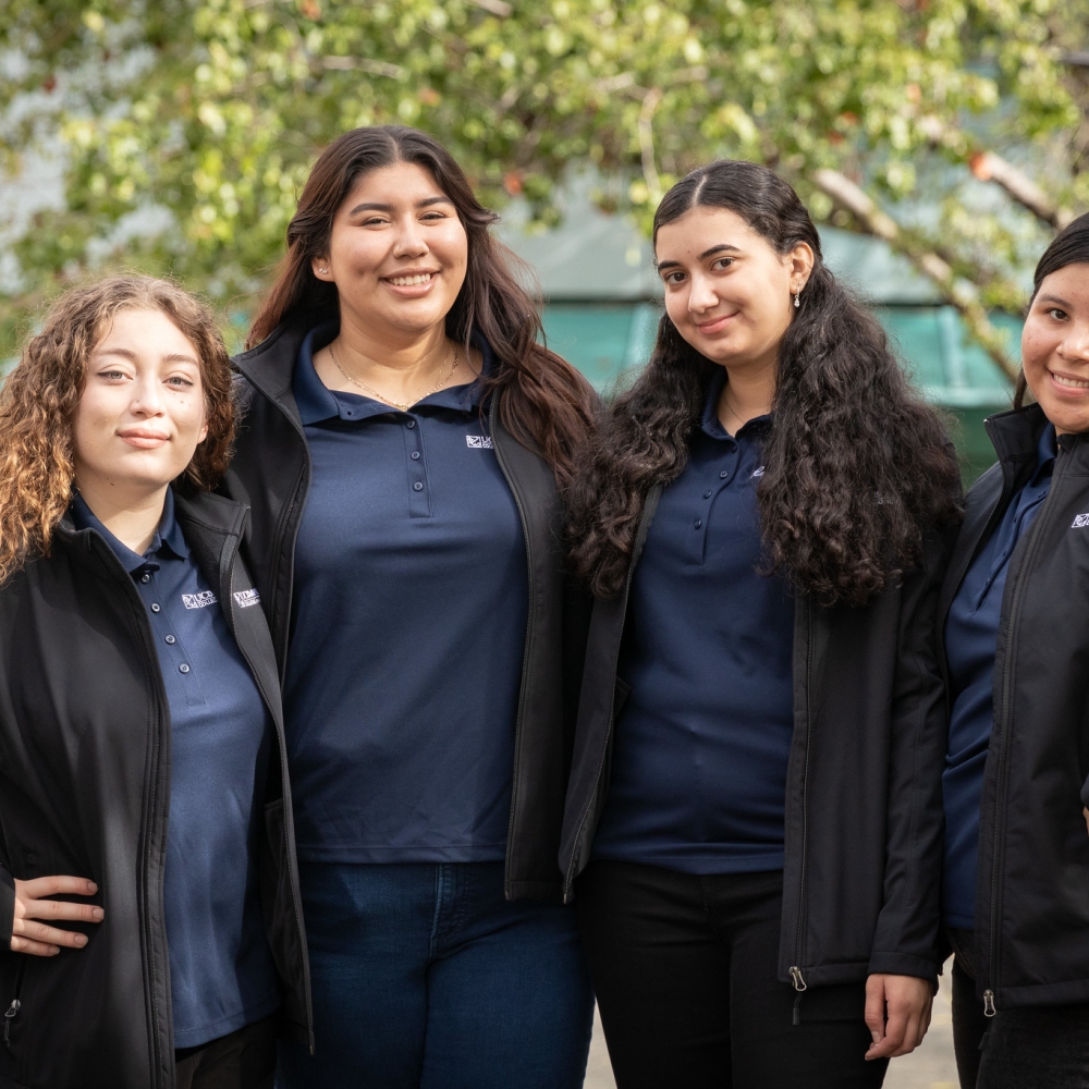 Four people with matching polo shirts stand together and pose for a photo outside