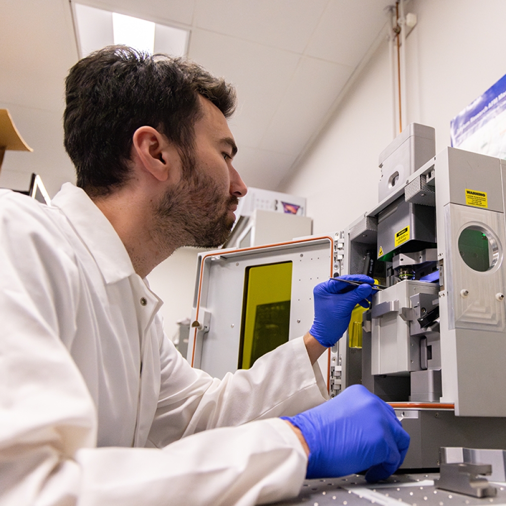 Calum Shelden wears PPR and works in a lab with a large microscope