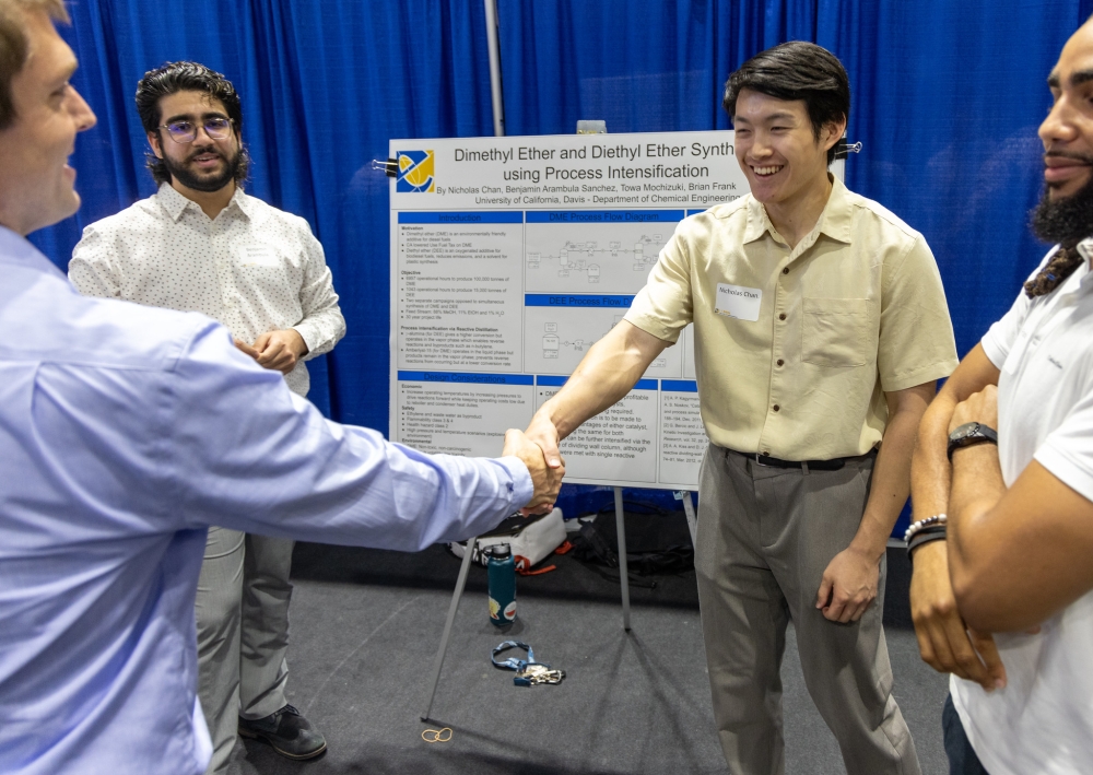 Two people shake hands in front of a poster presentation